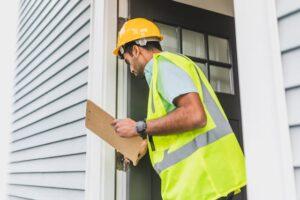 Person wearing a hard hat and vest holding a clipboard