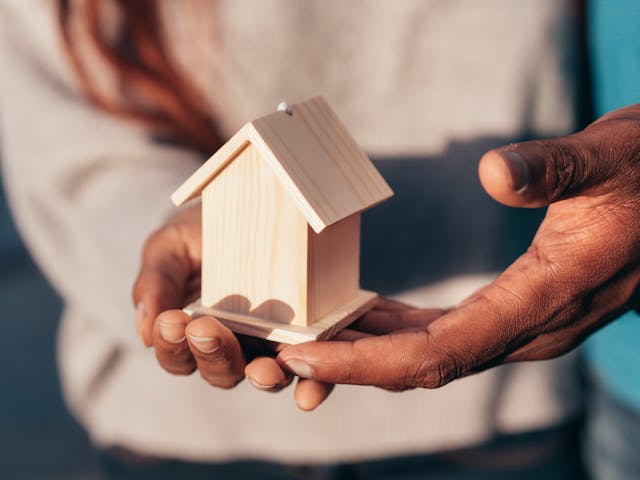 two people holding a wooden miniature house